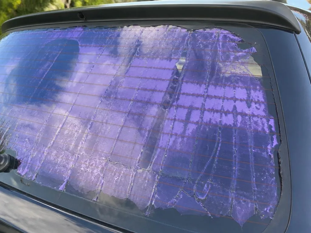 Old window tint bubbling and turning purple on a car rear window before removal